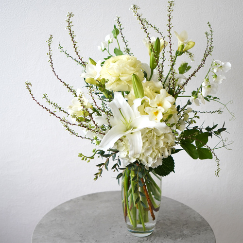白いユリと淡い黄色の花々を合わせた花瓶花