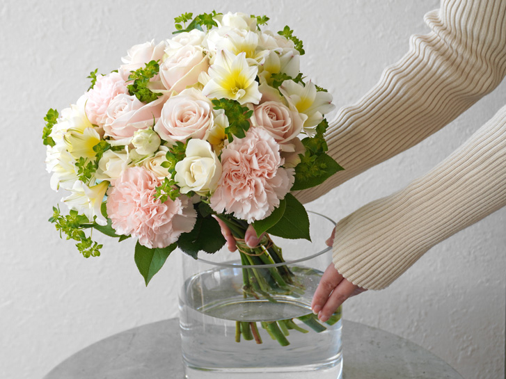 淡いピンクの大輪バラとカーネーションの花束を花瓶に入れる様子
